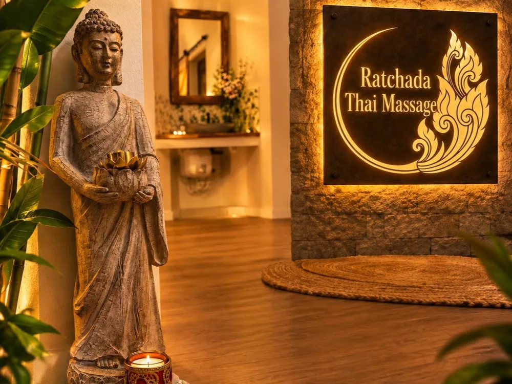 Entrada de Ratchada Thai Massage a Girona: Buda dret amb una espelma i el rètol retroil·luminat del centre